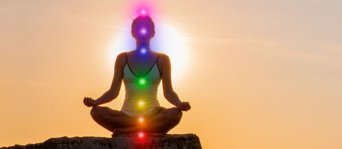 Pessoa em posição de meditação com os 7 pontos das chakras destacados