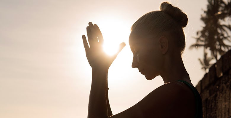 Mulher meditando com as mãos juntas em posição de meditação