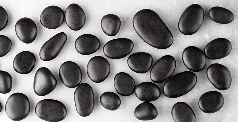 Várias pedras naturais de ônix preto rolado sobre uma mesa branca.