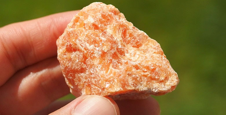 Pessoa segurando uma pedra de calcita laranja na mão.