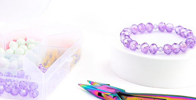 Mesa com maleta de cristais de vidro, alicate rainbow e uma pulseira elástica de cristal.