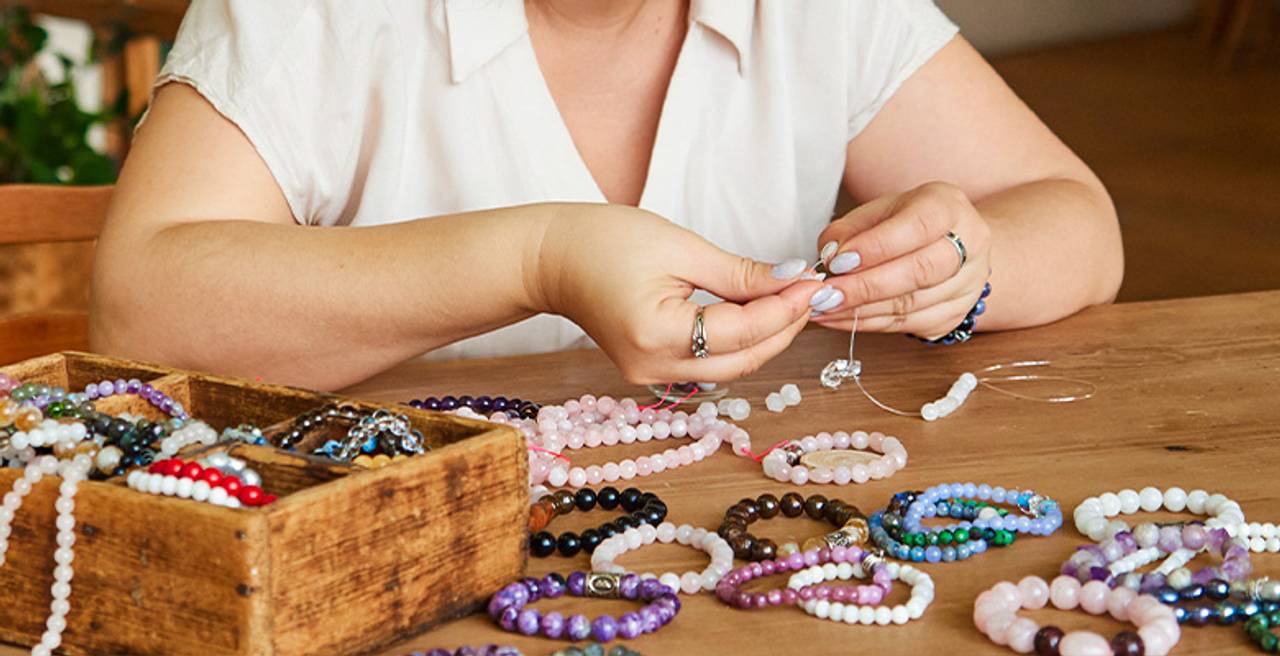 artesa montando diversas pulseiras de pedras naturais sobre mesa com fios em pedras