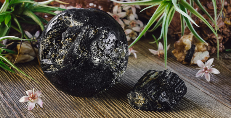 Rocha natural de turmalina negra em bastão e esfera em cima de mesa com flores